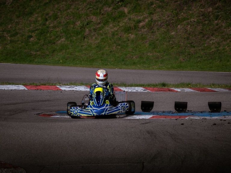 Ein Go-Kart-Fahrer auf einer Rennstrecke mit einer grünen Landschaft im Hintergrund.